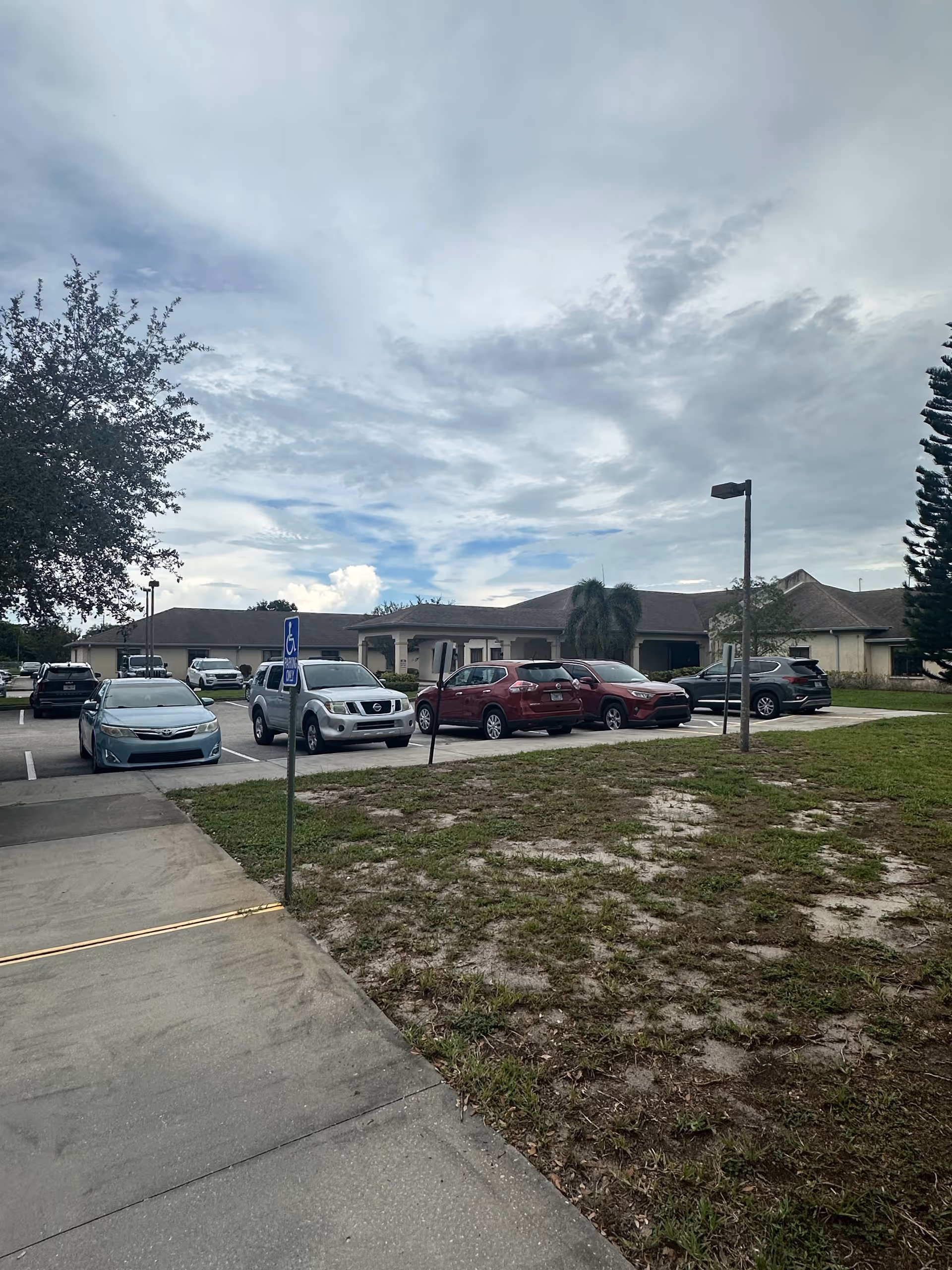 Front view of a senior living facility with parked cars and a handicapped parking sign.