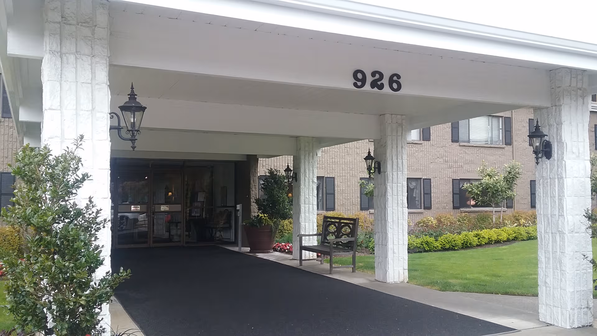 Entrance to Delaware Plaza Assisted Living Community, featuring white pillars, a covered porte-cochère, and landscaping.