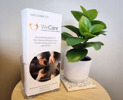 A brochure display labeled WeCare beside a green potted plant on a wooden table.
