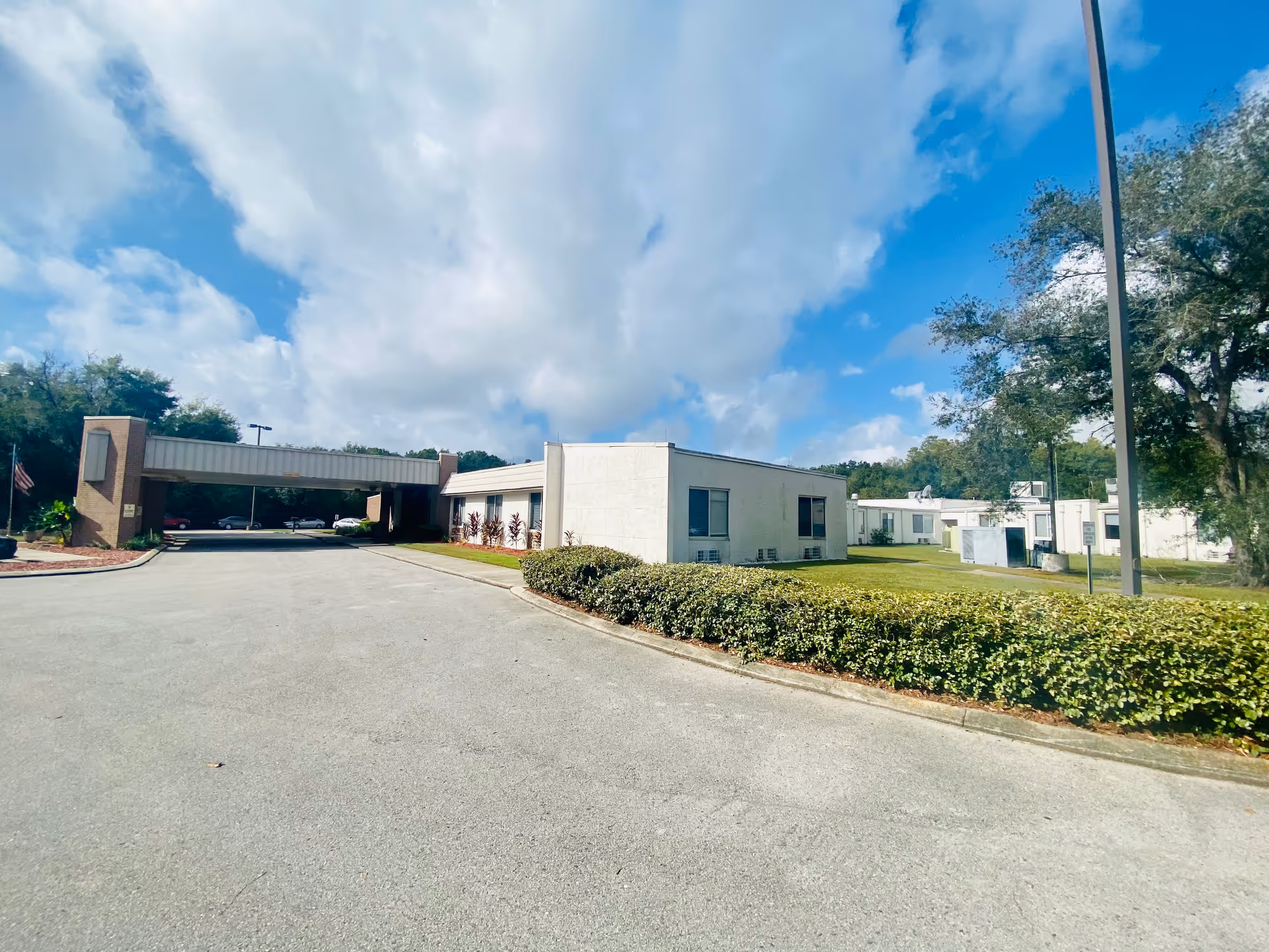 Exterior view of Carrollwood Care Center showing a driveway, hedges, and low white buildings.