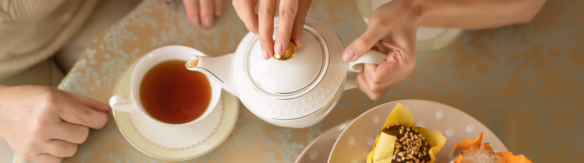 People share tea and cake around a table with a teapot and cup.