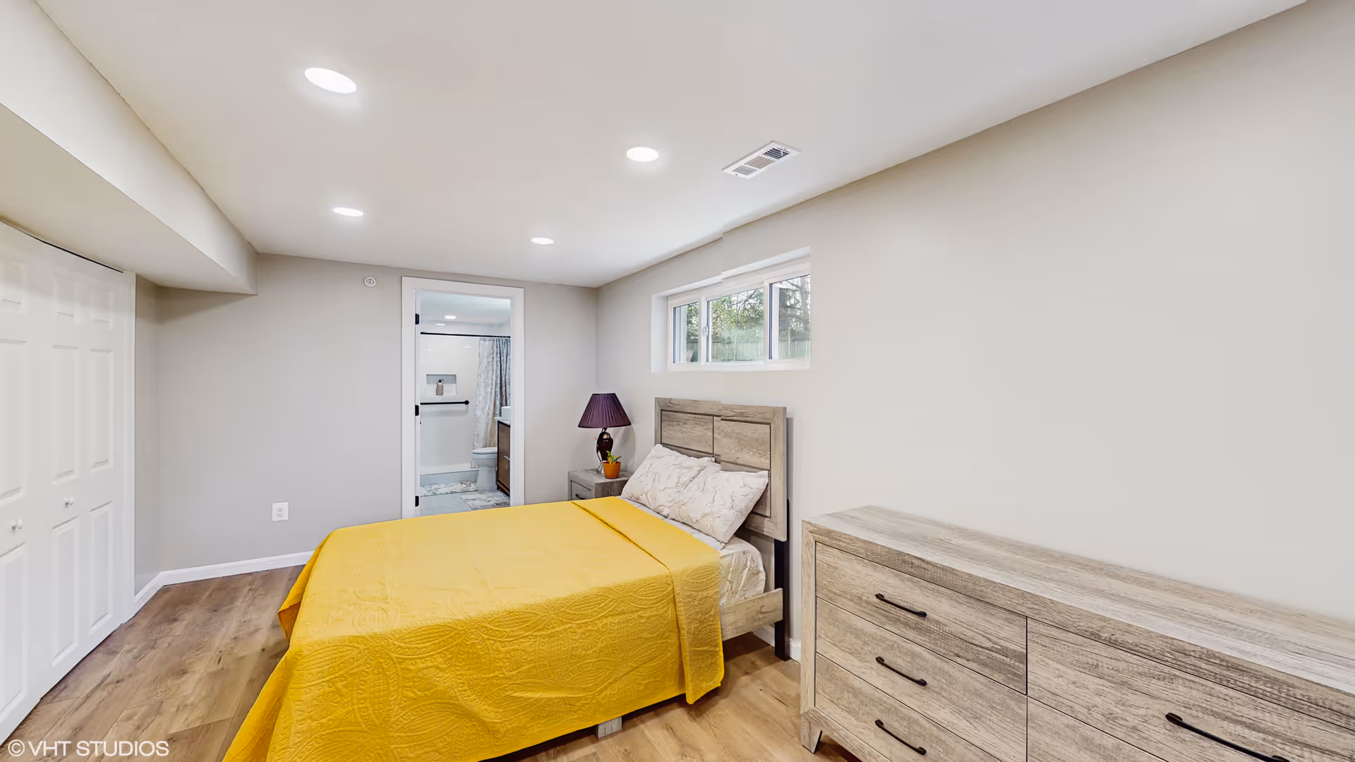 Neutral bedroom with a yellow quilted bed, wood dresser, and doorway to bathroom.