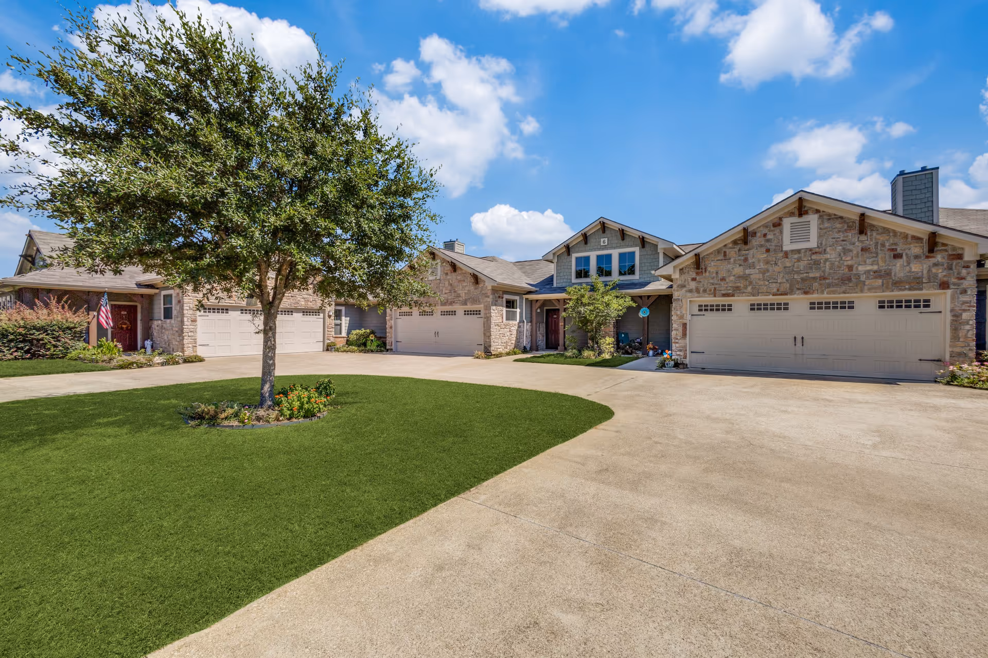 Front view of a residential-style senior living facility with stone facade, garages, and a lawn.