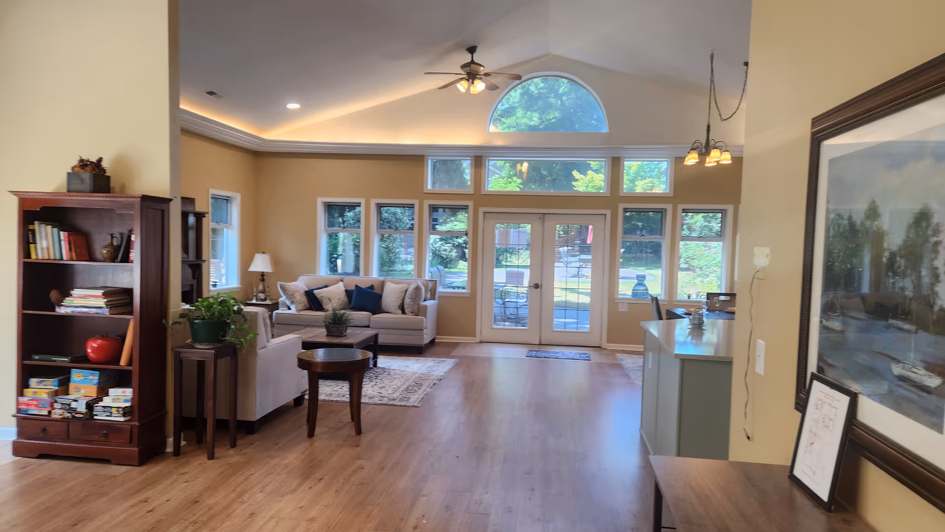 Bright living room at North Gate Senior Care with couches, coffee table, shelves, and windows.
