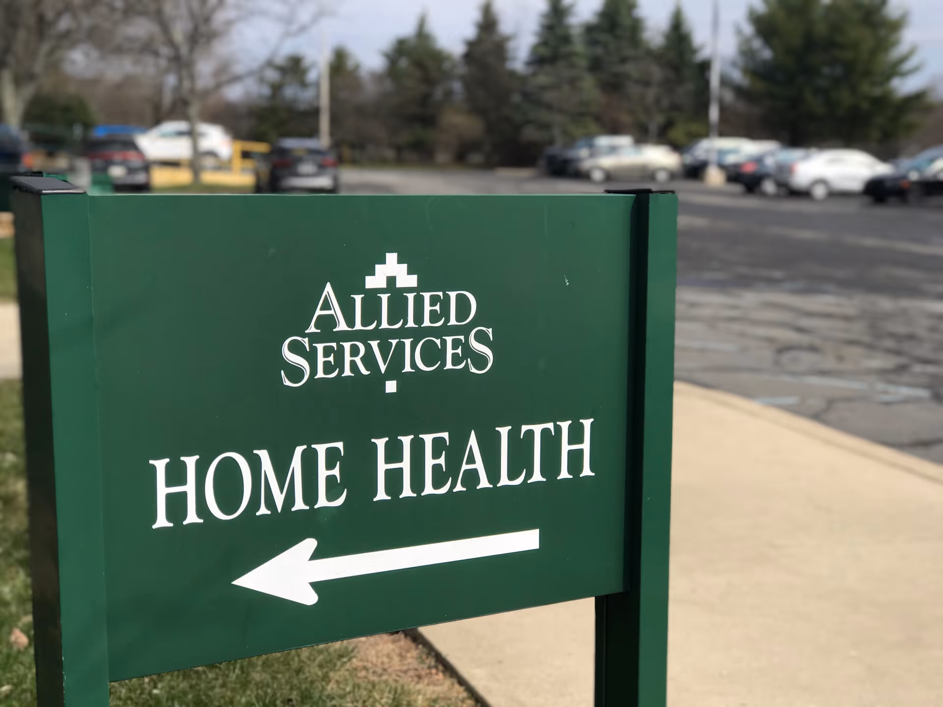 Green Allied Services Home Health sign with arrow in a parking lot