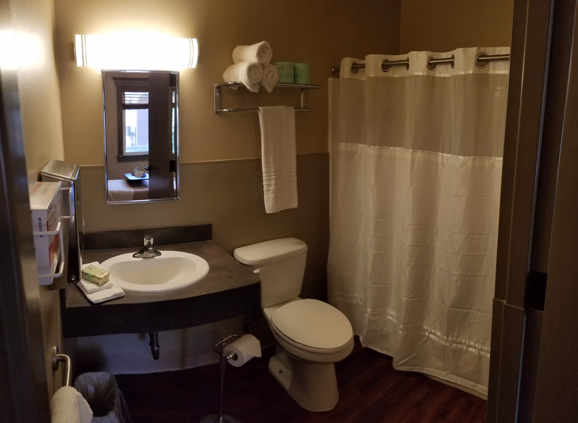 Compact bathroom with sink, toilet, shower curtain, mirror, and folded towels.