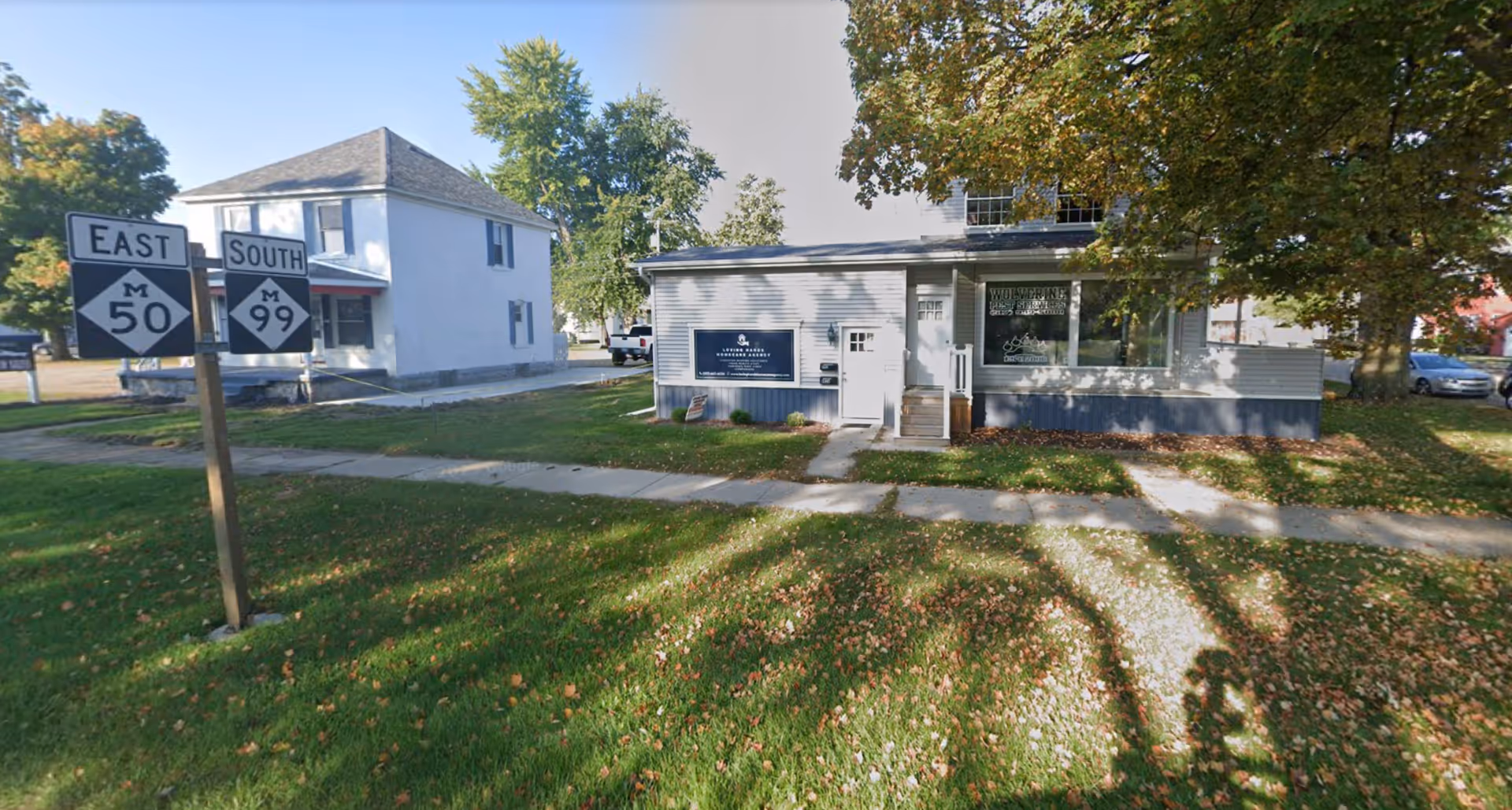 Small single-story building with a sign and large front windows beside a tree-lined sidewalk.