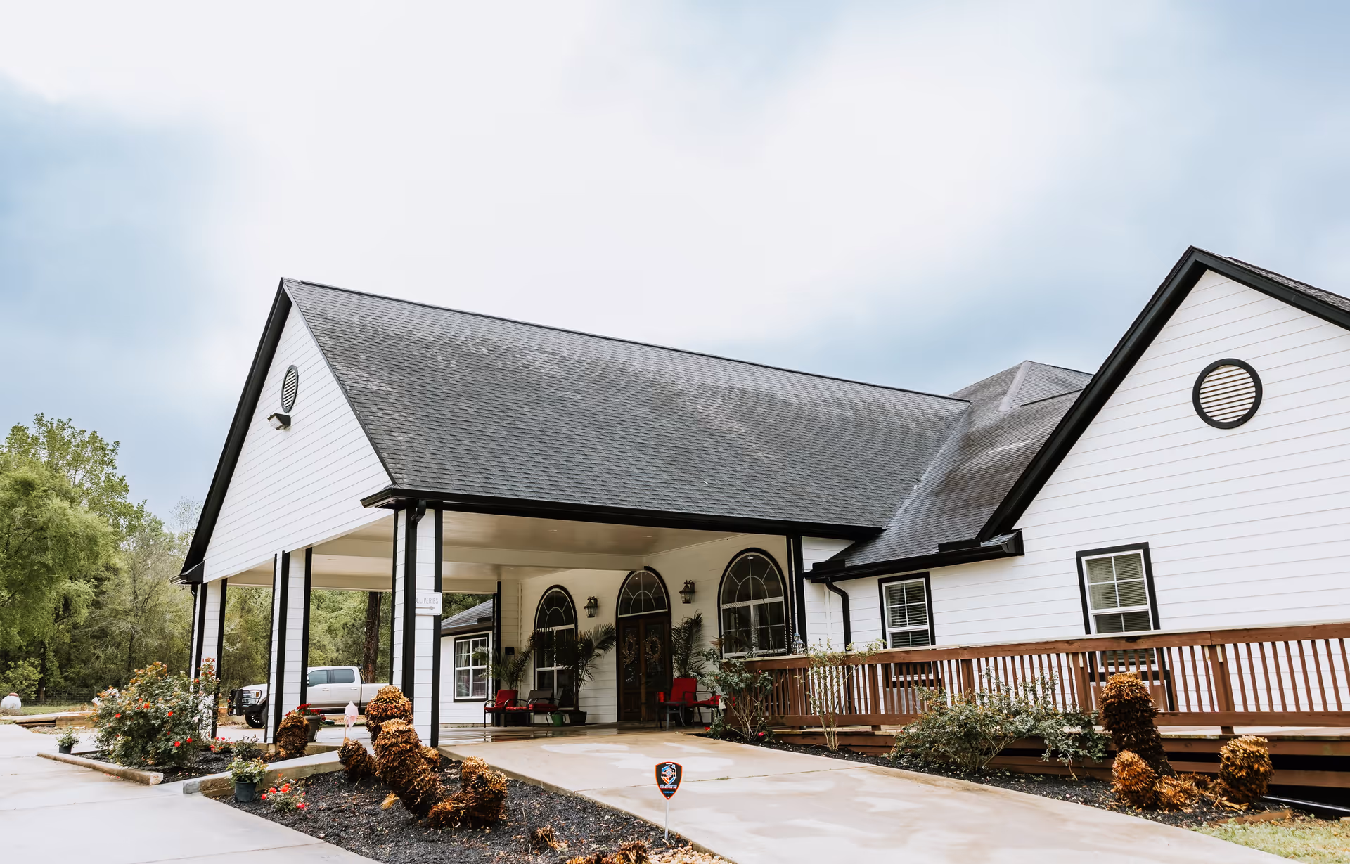 Front entrance of a white single-story senior living facility with a covered porte-cochère and landscaped driveway.