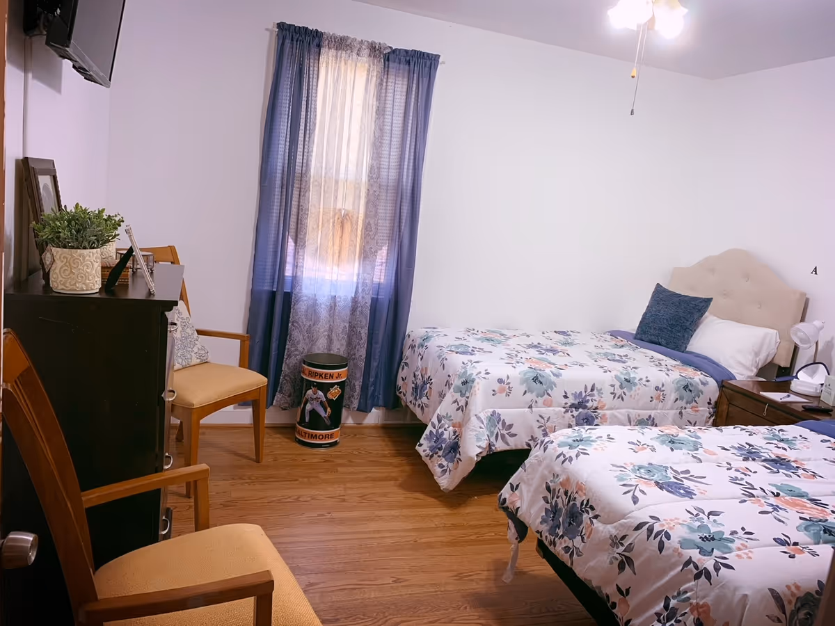 Two twin beds with floral bedding in a small senior living facility bedroom.