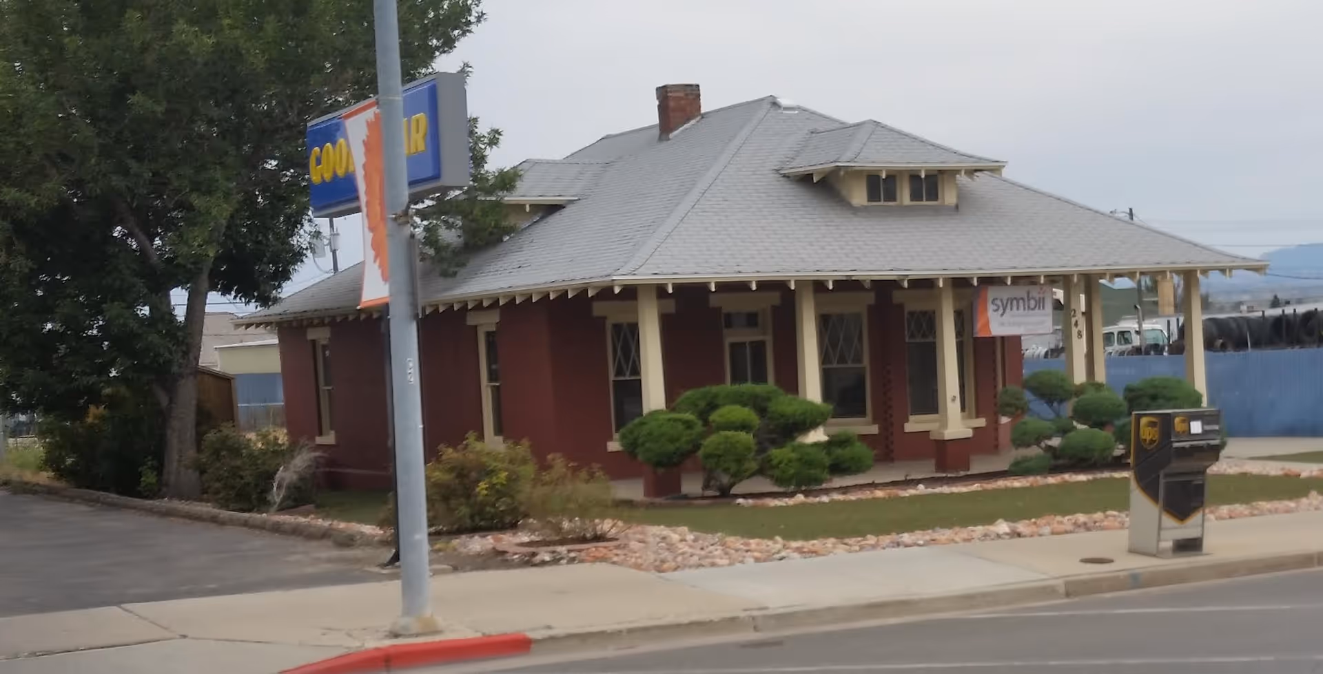 A small red-brick building with a covered front porch and manicured shrubs.