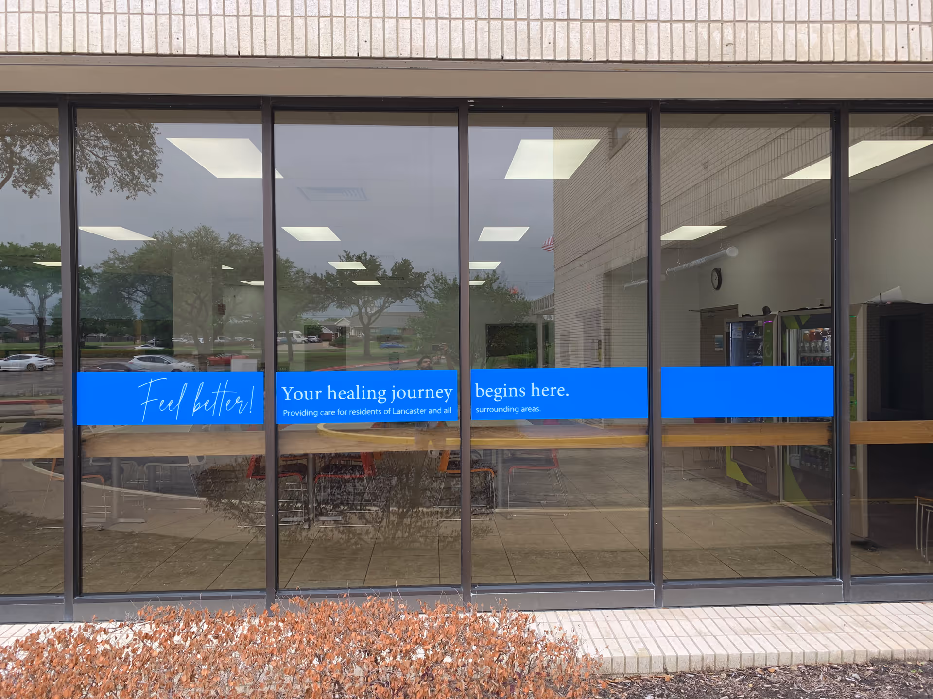 Glass storefront with blue banners across windows and reflections of trees outside.