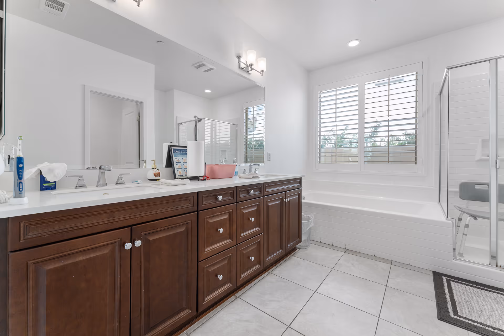 Bright bathroom with double sinks, dark wood vanity, tub, glass shower, and a window.
