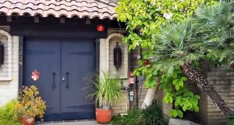 Blue double doors with stone facade, surrounded by potted plants and greenery.