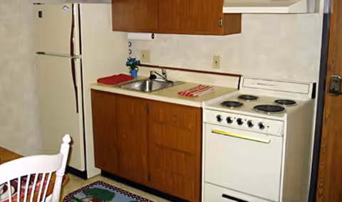 Compact kitchen with fridge, sink, stove, and wooden cabinets in a senior living unit.