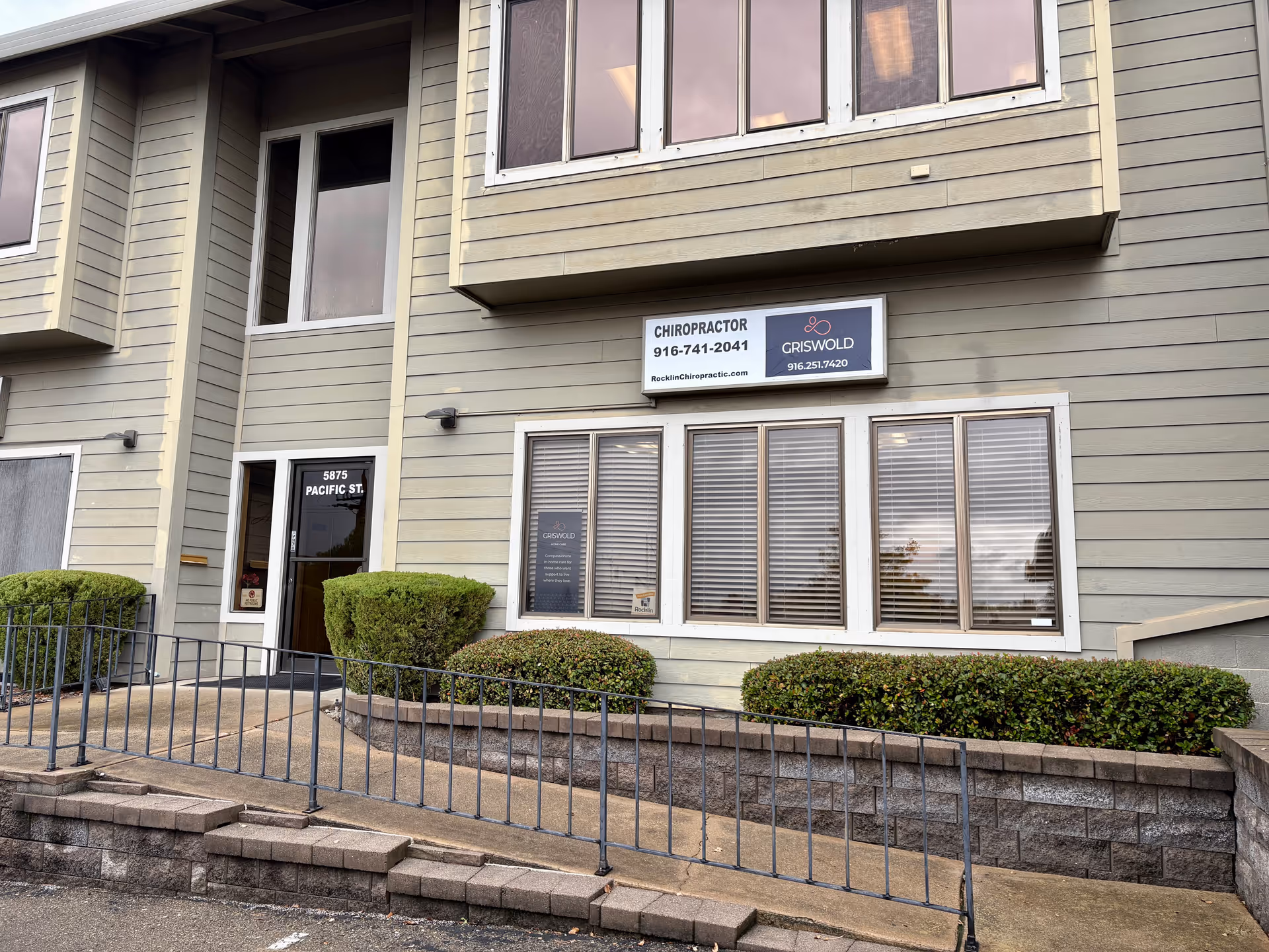 Exterior view of a beige building with windows, signage, and a ramp entrance.