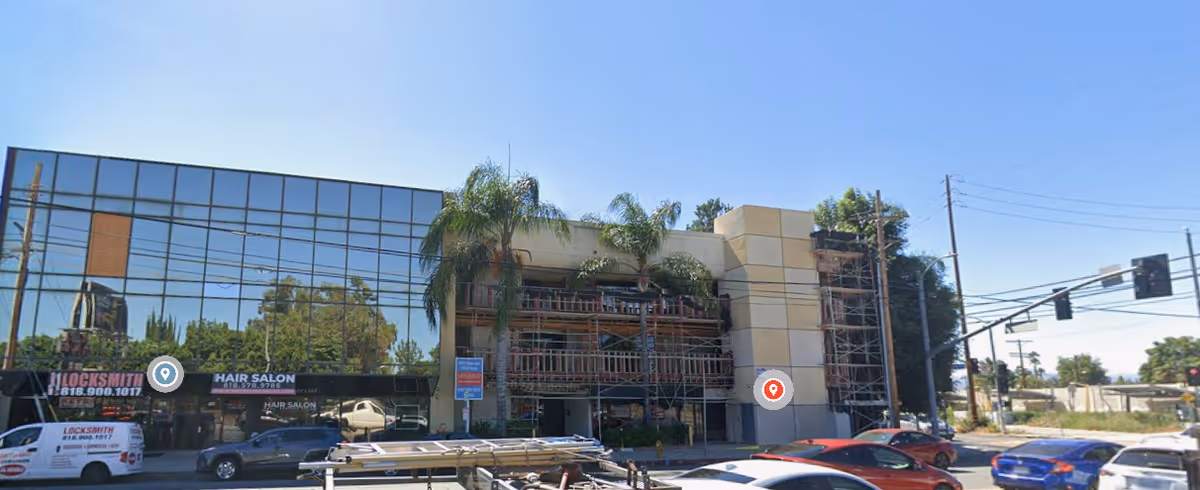 Street view of a modern building with glass facade, storefronts, and construction scaffolding.