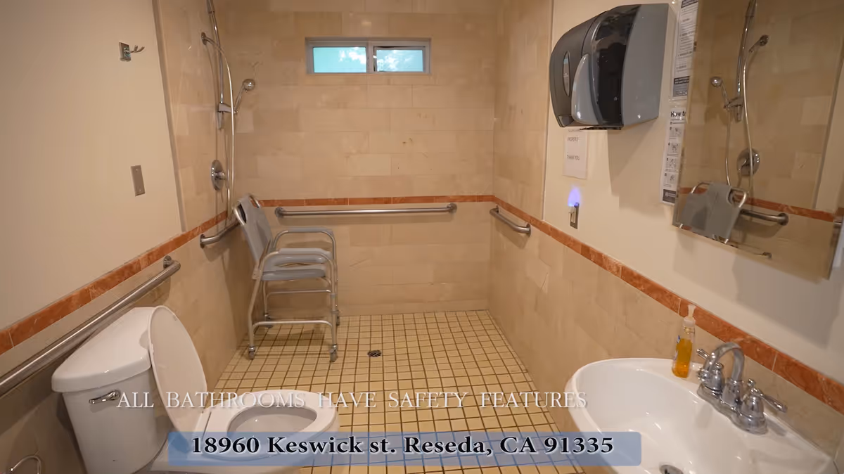 Accessible bathroom with toilet, sink, mirror, grab bars, shower chairs and a handheld showerhead.