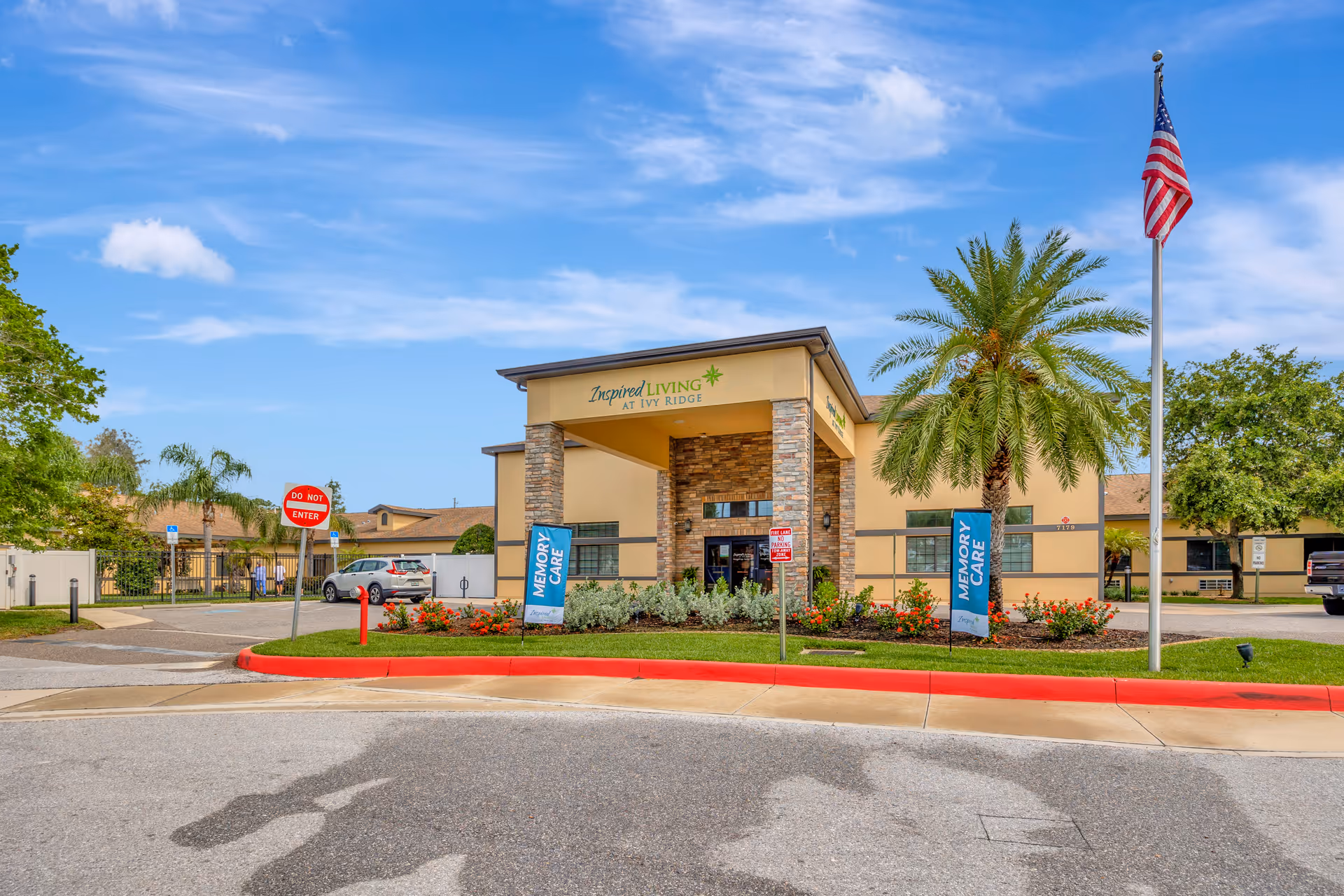Front exterior view of Inspired Living at Ivy Ridge entrance with palm trees and flag