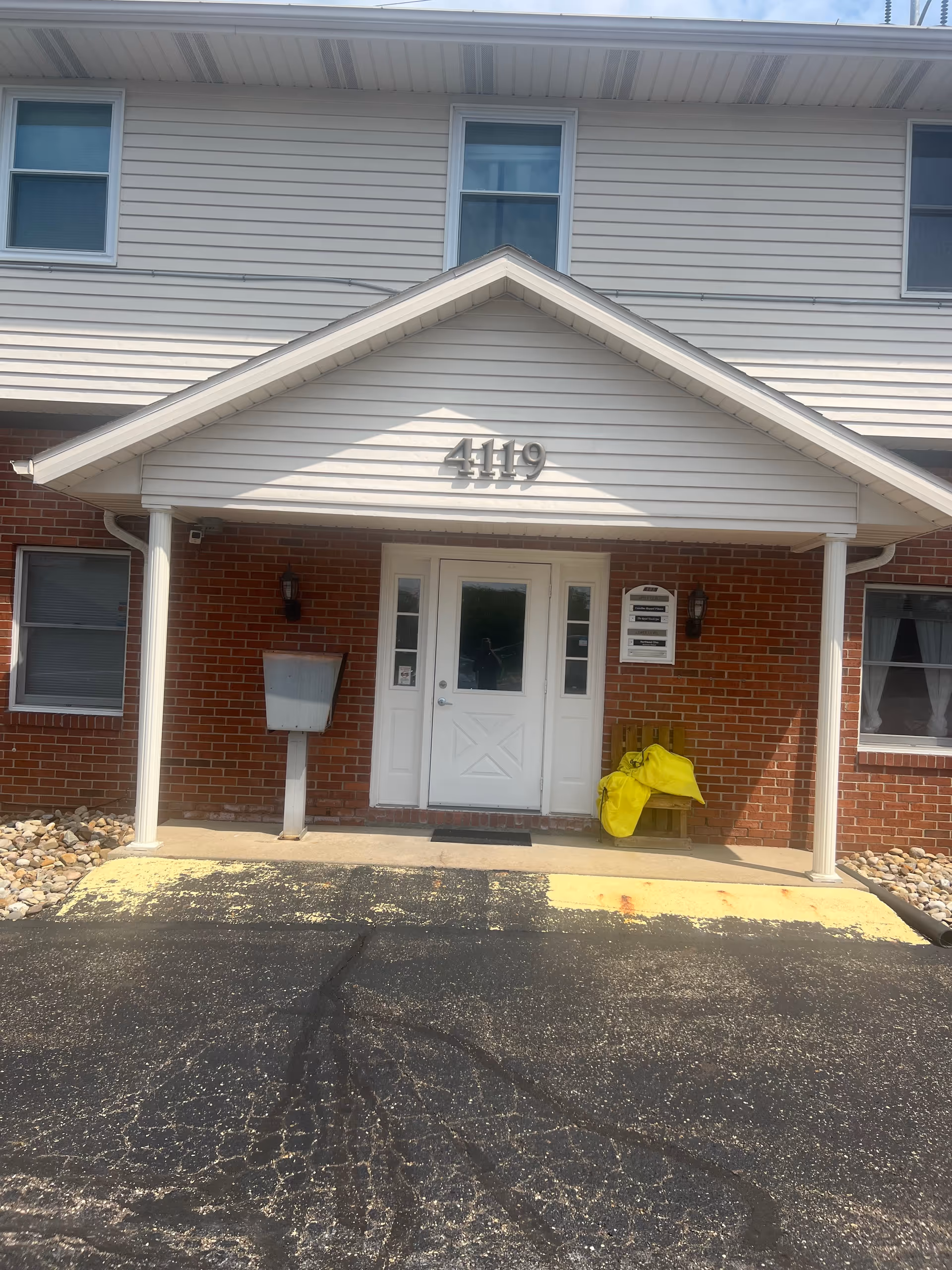 Exterior view of brick facility entrance labeled 4119 with white door and peaked overhang.
