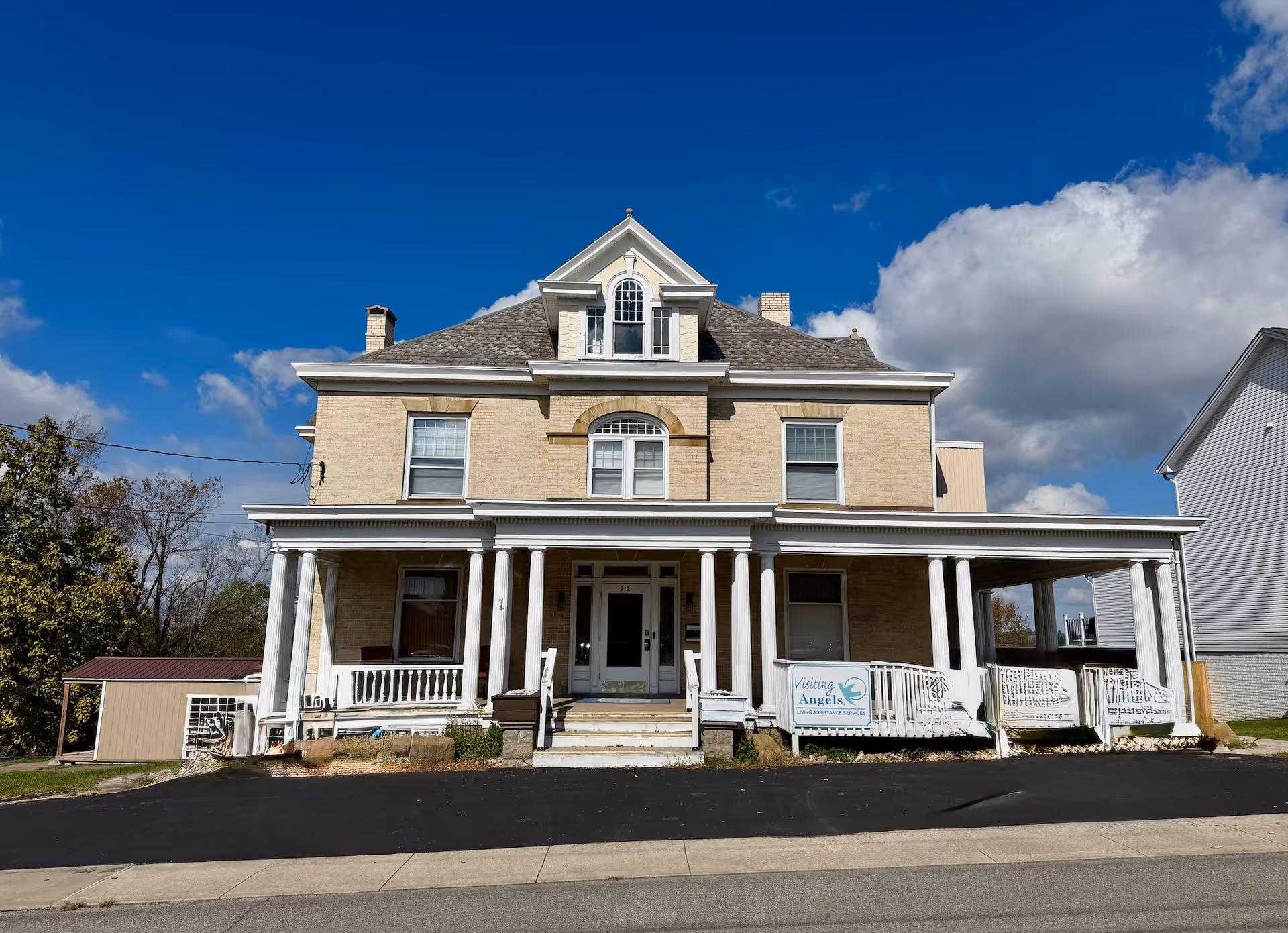 Two-story beige brick house with white porch columns and a banner on the railing.