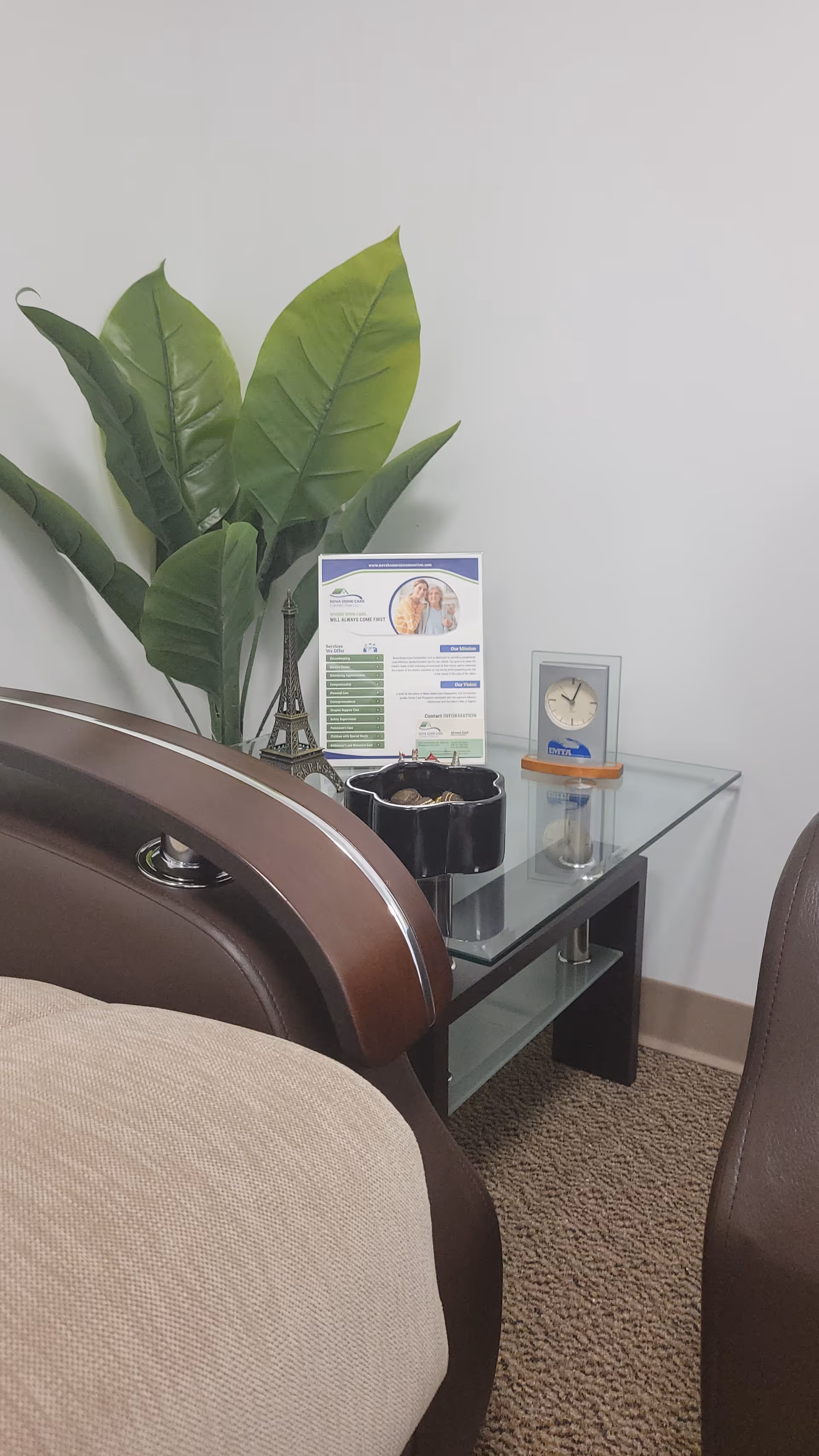 Corner of a treatment room with a glass side table, plant, and clock.