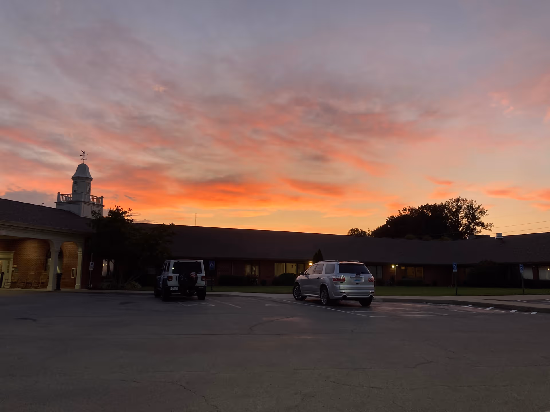 Sunset skies over a single-story nursing facility exterior with a parking lot in the foreground.