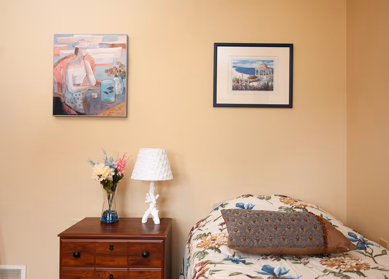 Cozy bedroom in a senior living facility with floral bedspread and wall art.