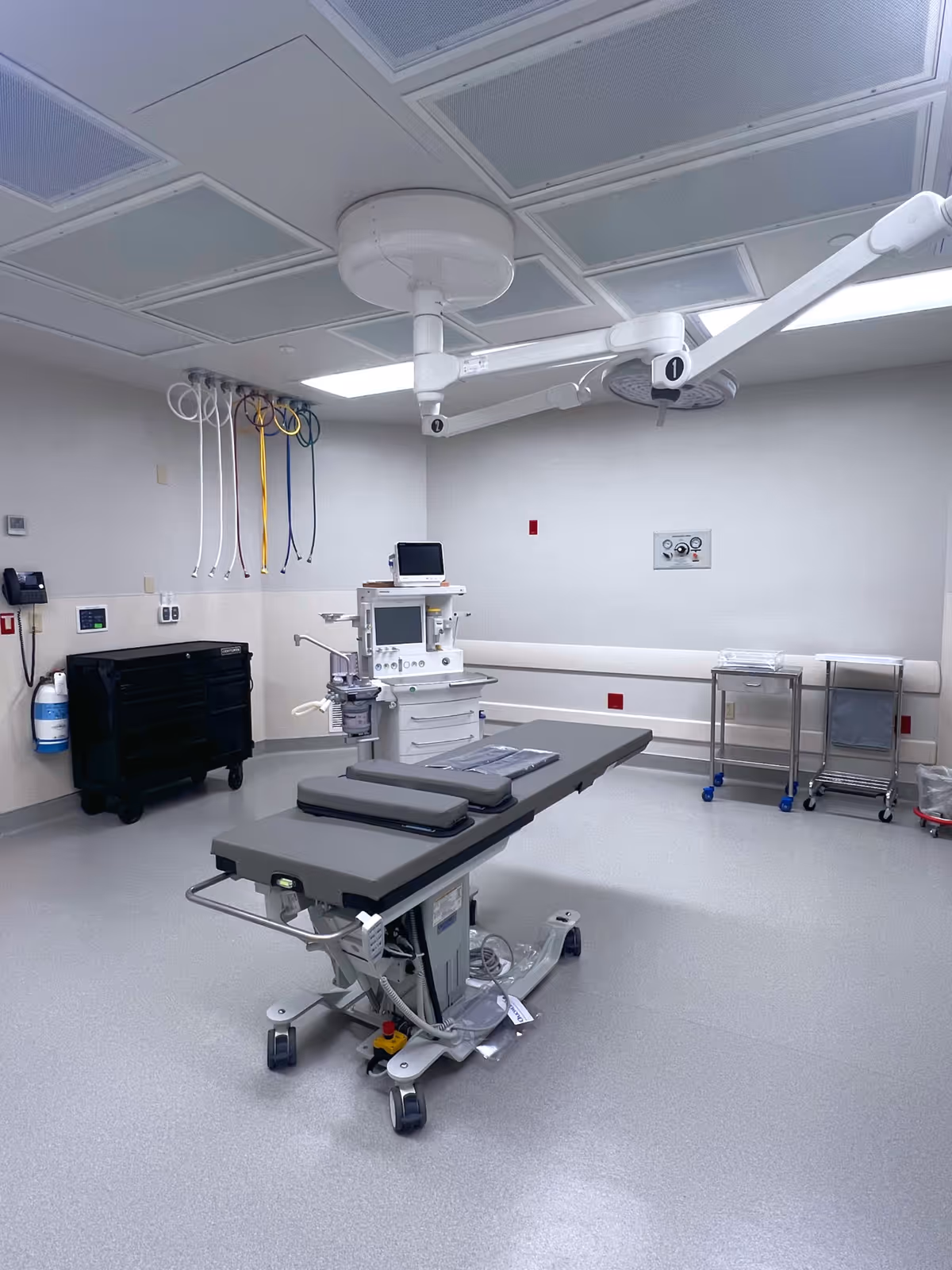 Sterile operating room with a surgical table, overhead lights, and anesthesia equipment.