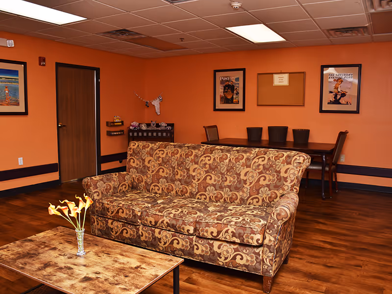 Patterned sofa and coffee table in a warm-toned common living area with a dining table and framed art on the walls.