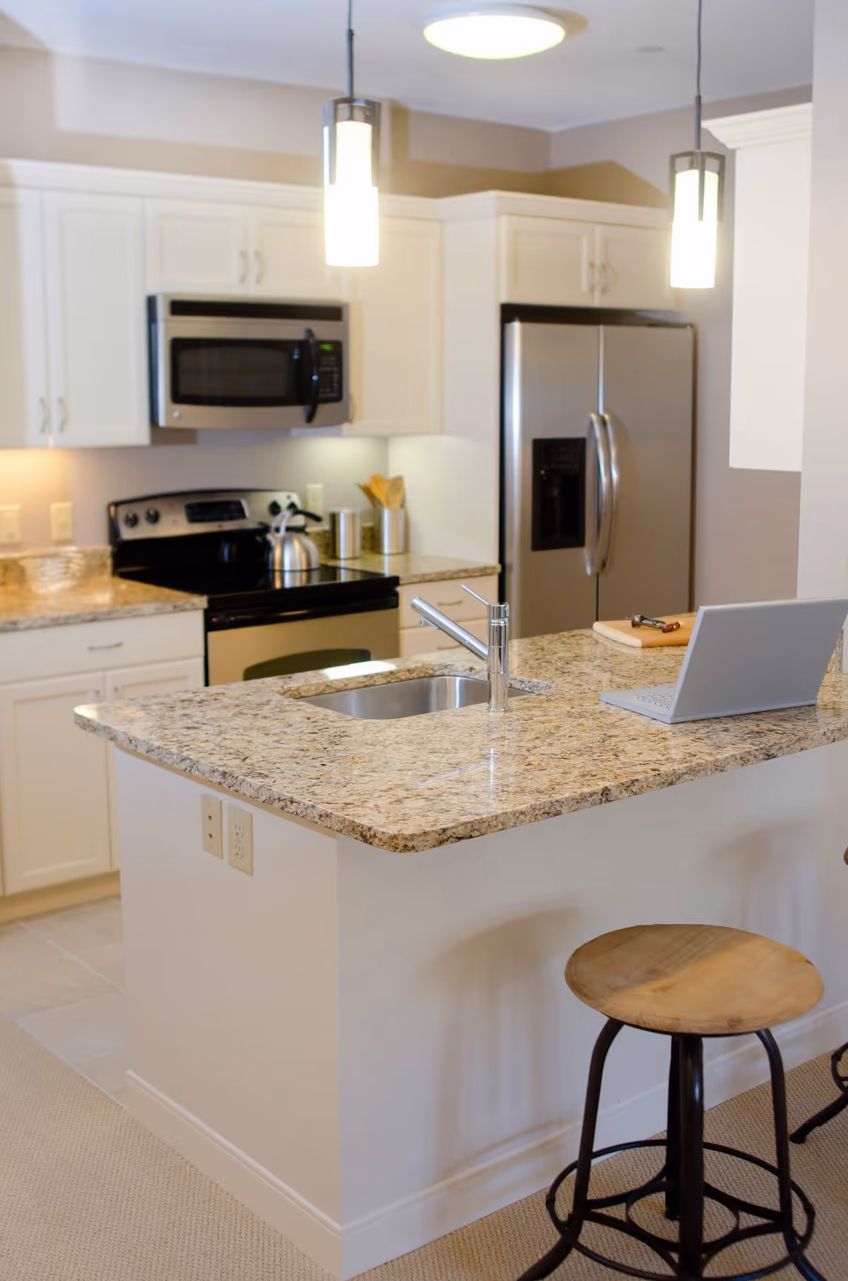 Modern kitchen with island, granite countertop, sink, appliances, and laptop on counter