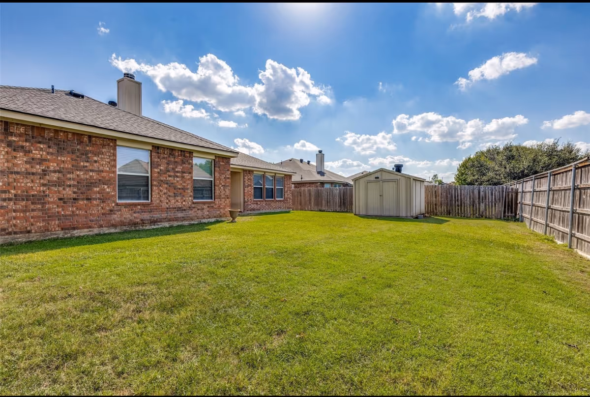 Backyard of Heritage Vue Assisted Living: brick building, fenced lawn, shed, and blue sky.