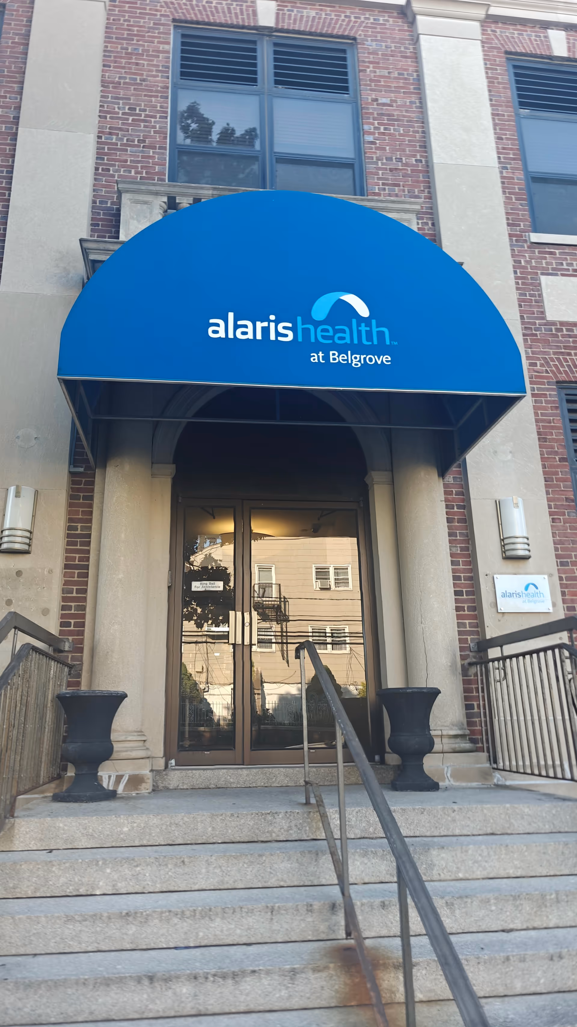 Front entrance of a brick building with a blue curved awning reading Alaris Health at Belgrove.