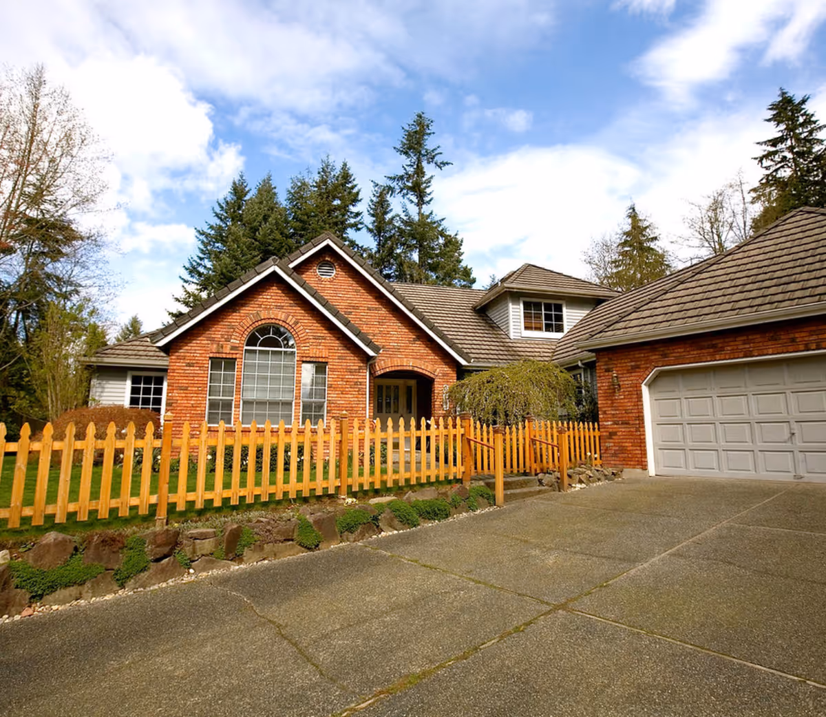 Front view of a brick house with a wooden picket fence and driveway.