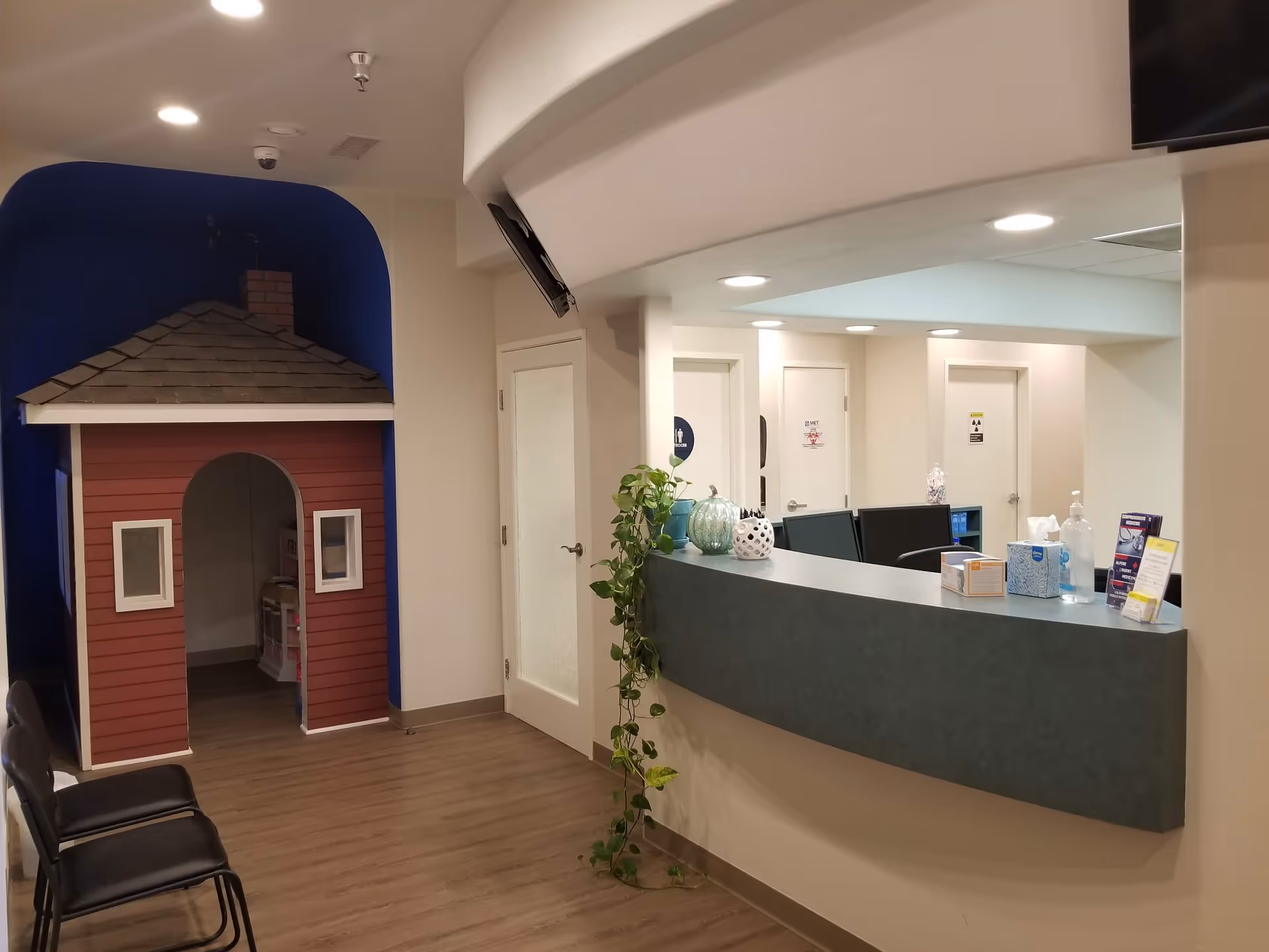 Lobby reception area with curved desk, a plant, and a red playhouse against a blue wall.