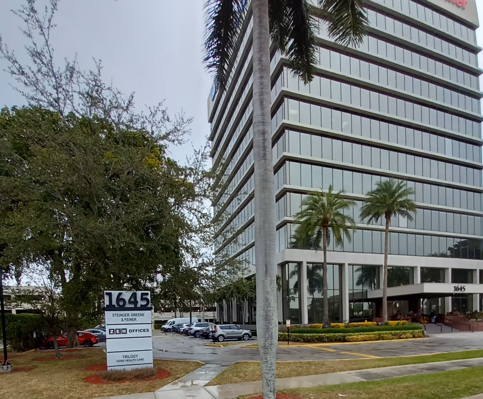 Tall glass-front office building with palm trees and a street sign.