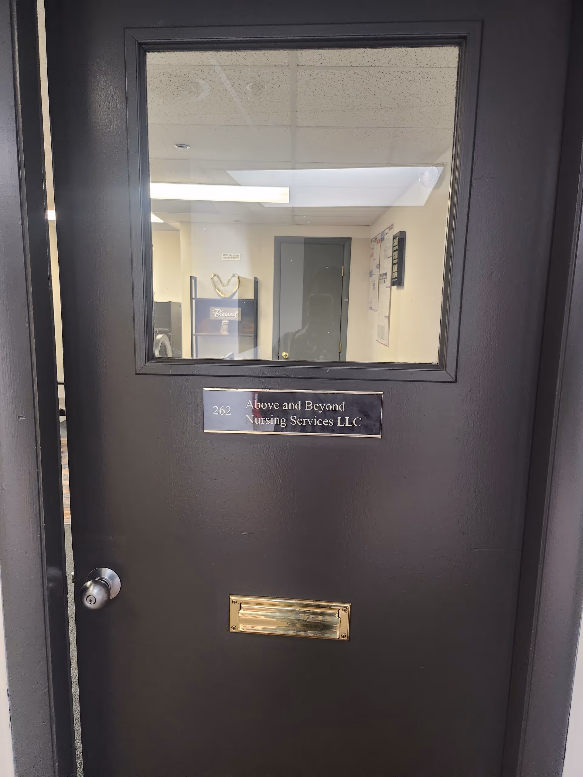 Dark door with window shows hallway and a plaque reading Above and Beyond Nursing Services LLC.