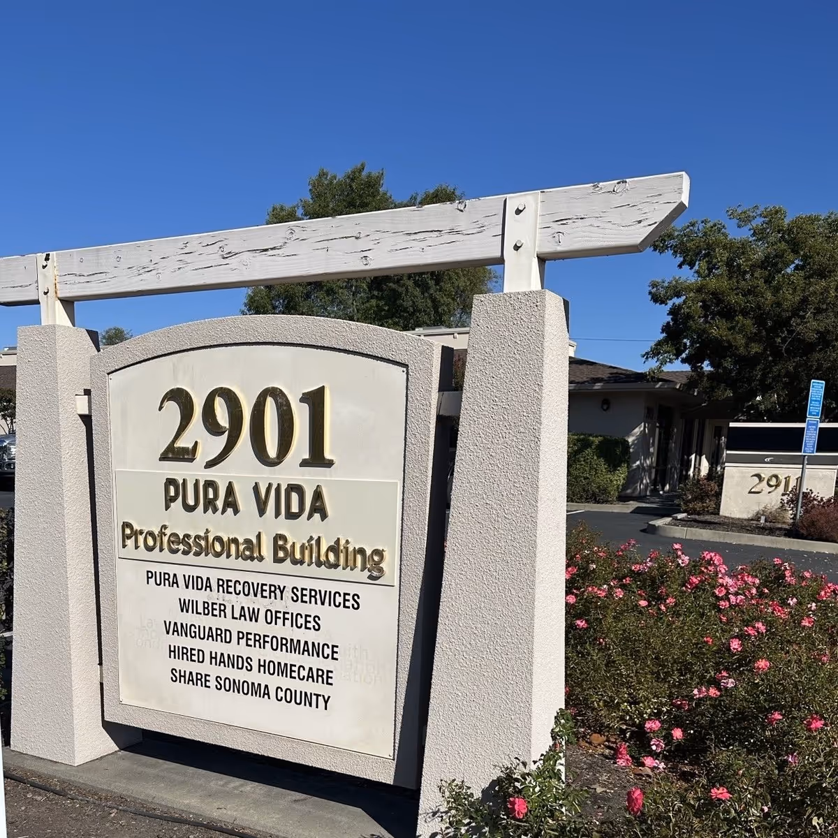 Exterior sign reading 2901 Pura Vida Professional Building with pink flowering shrubs nearby.