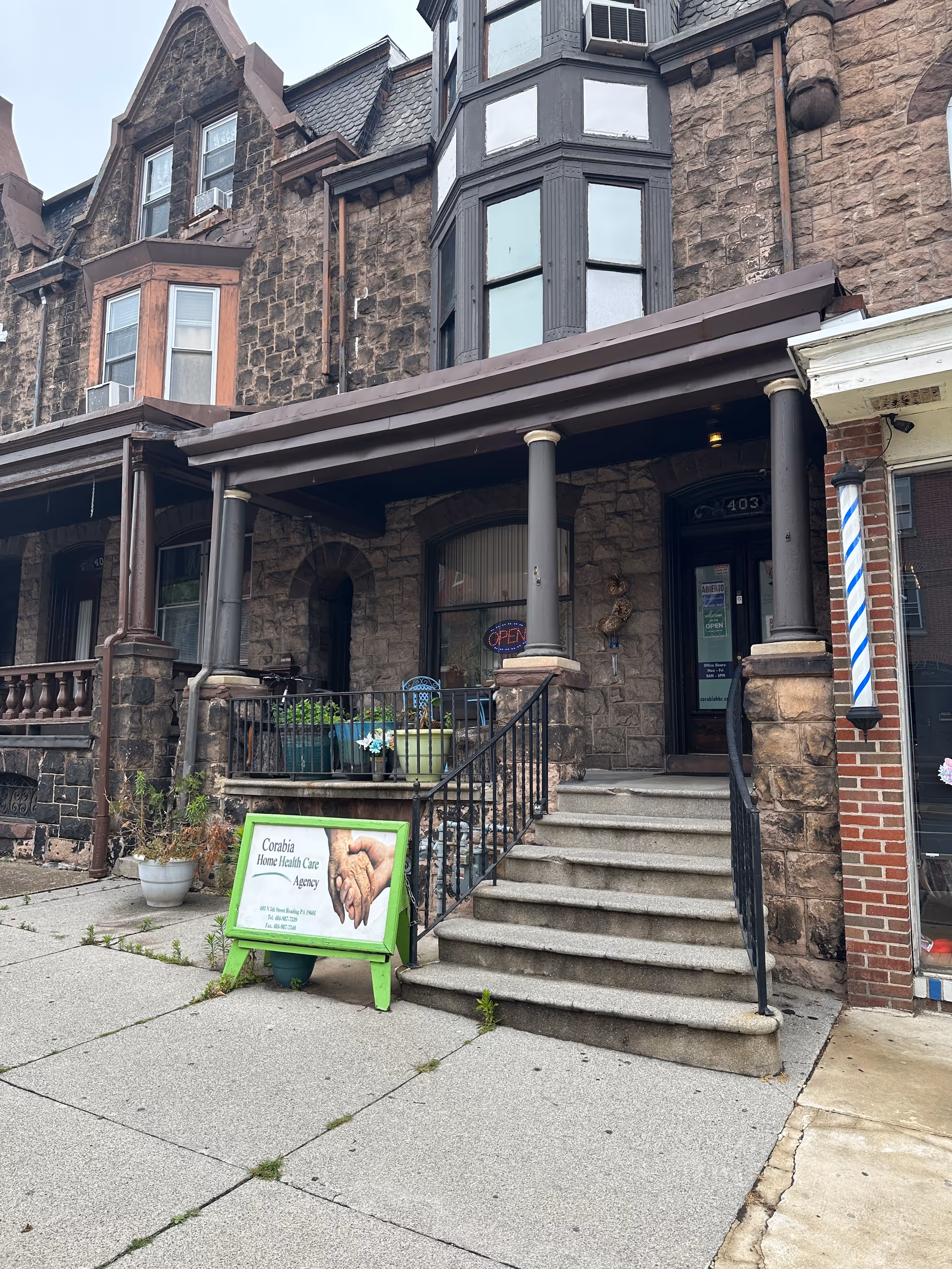 Stone-clad building front with entrance stairs, porch columns, and a green signboard.