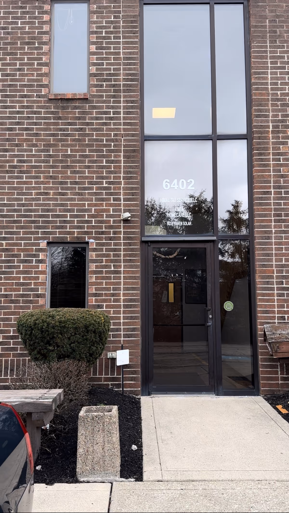 Brick facade with tall glass entry door and large window, 6402 address, and nearby shrub.
