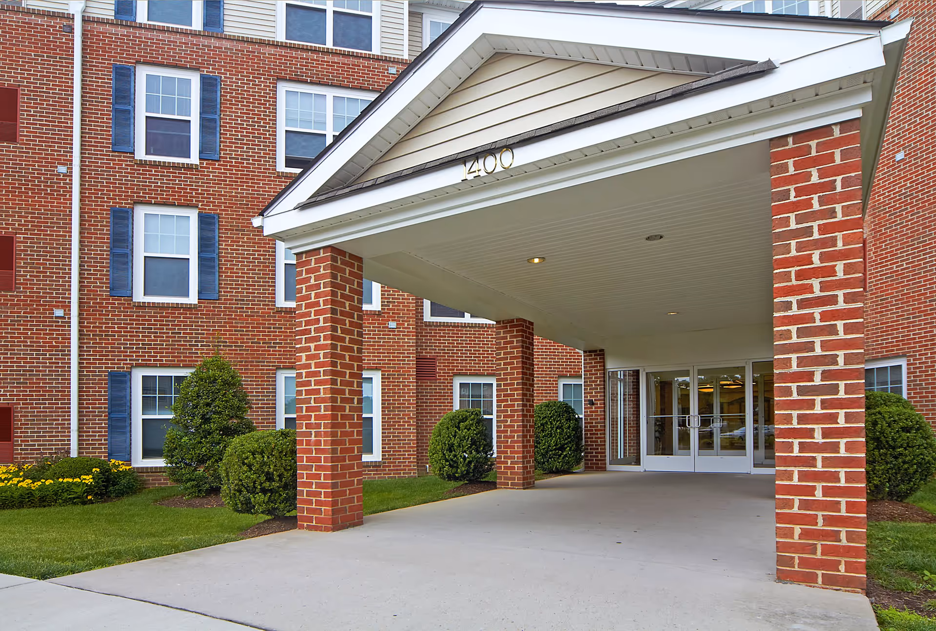 Covered brick entrance with columns and glass double doors at the front of a multi-story red brick building.