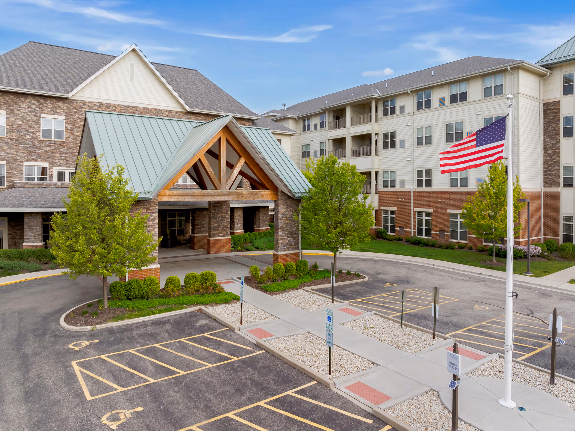 Exterior view of Deer Park Village senior living facility with entrance canopy, parking, and American flag.