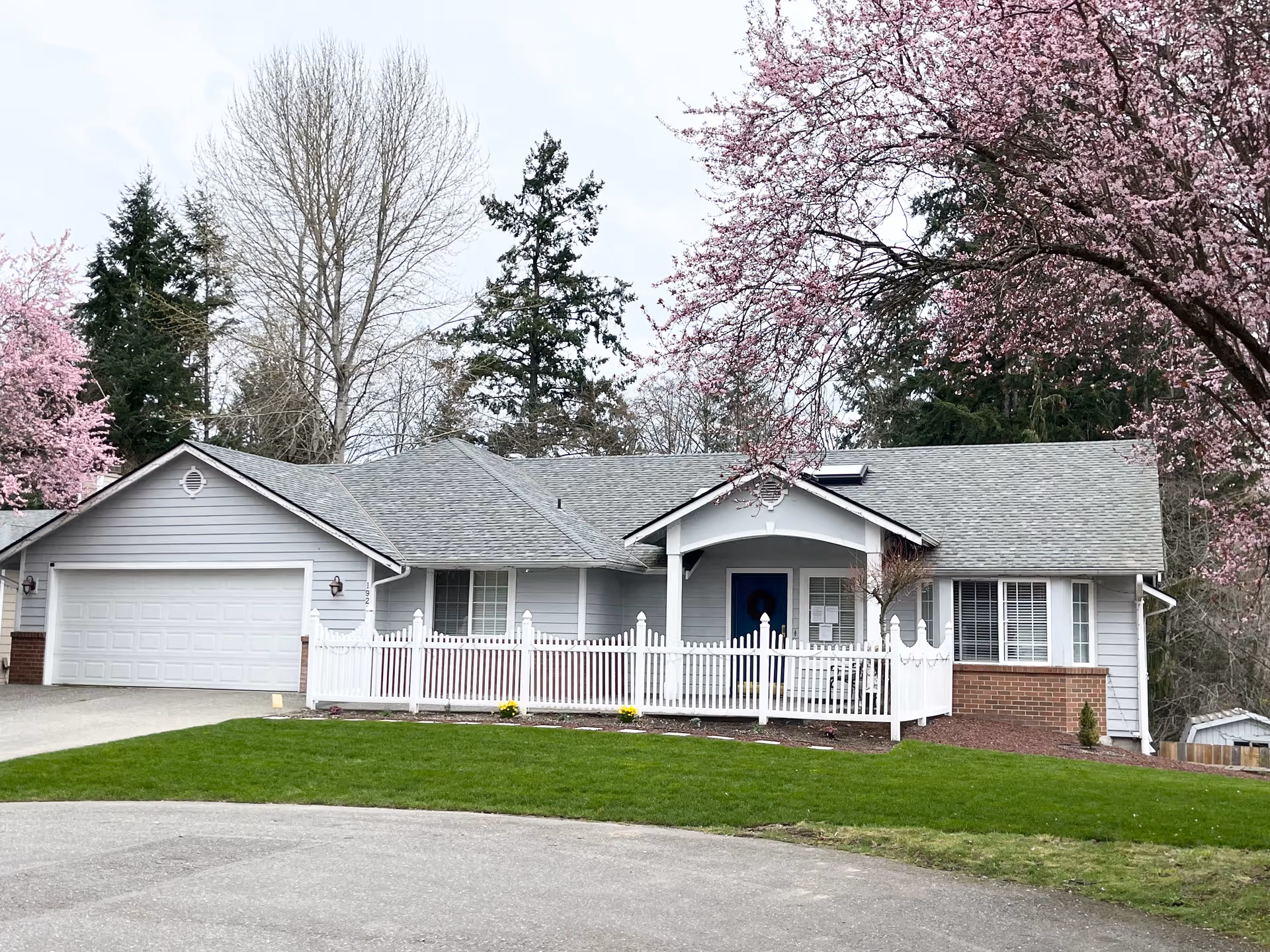 Front view of a Loving Care facility house with a white picket fence and blossoming trees.