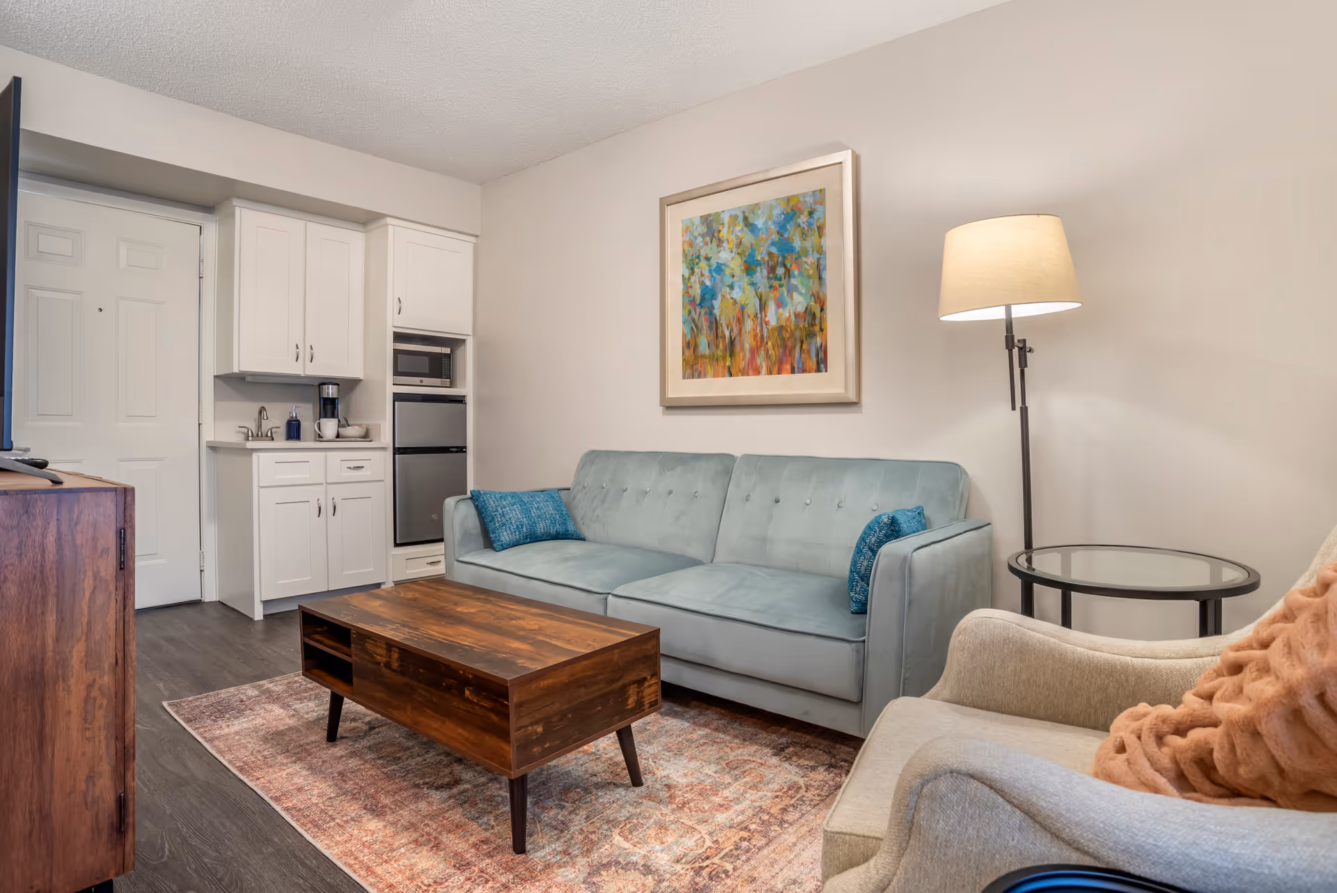 Cozy living room in a senior facility with sofa, chairs, coffee table, and kitchenette.