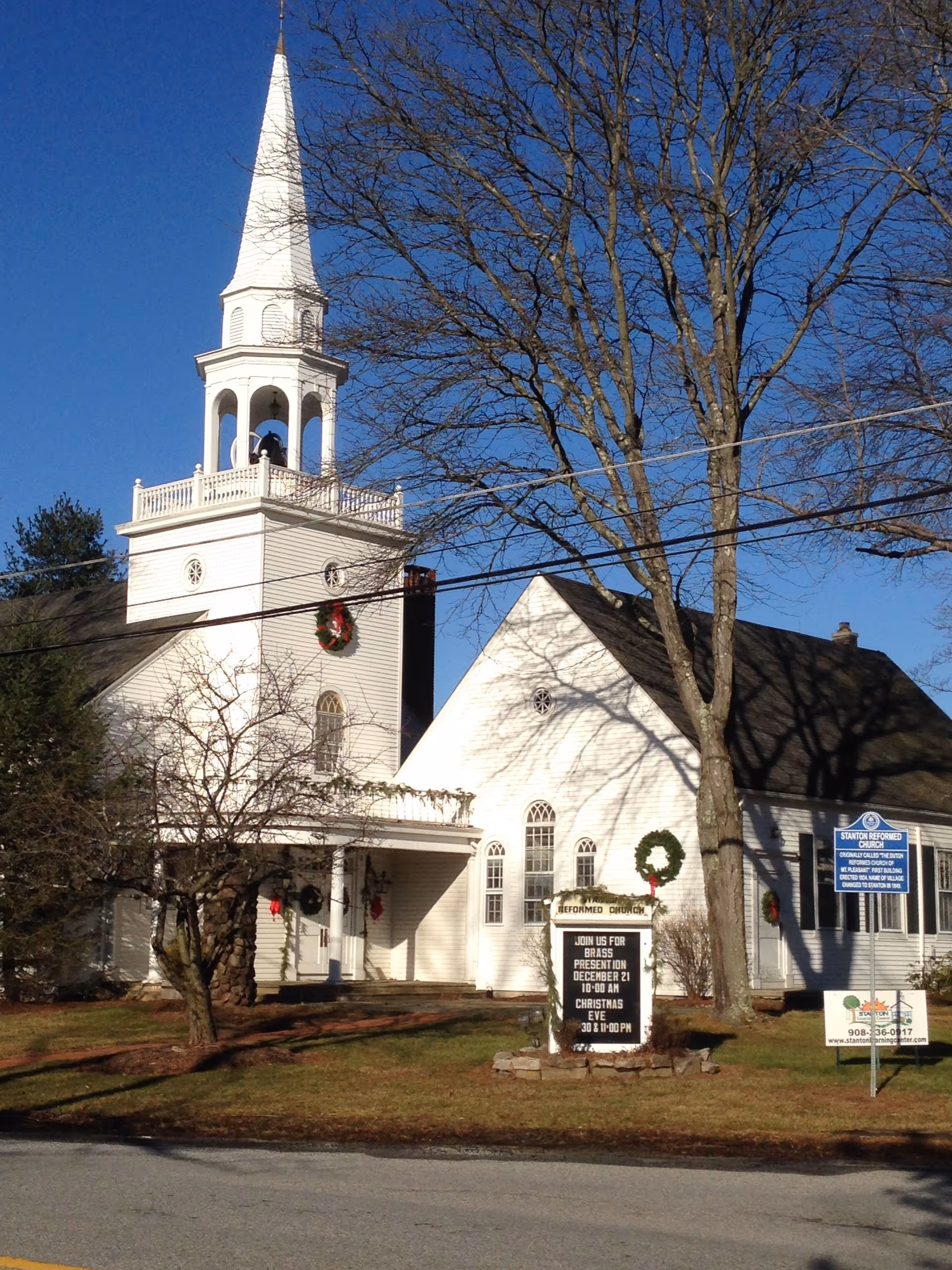 Front of a white church with tall steeple and bare trees
