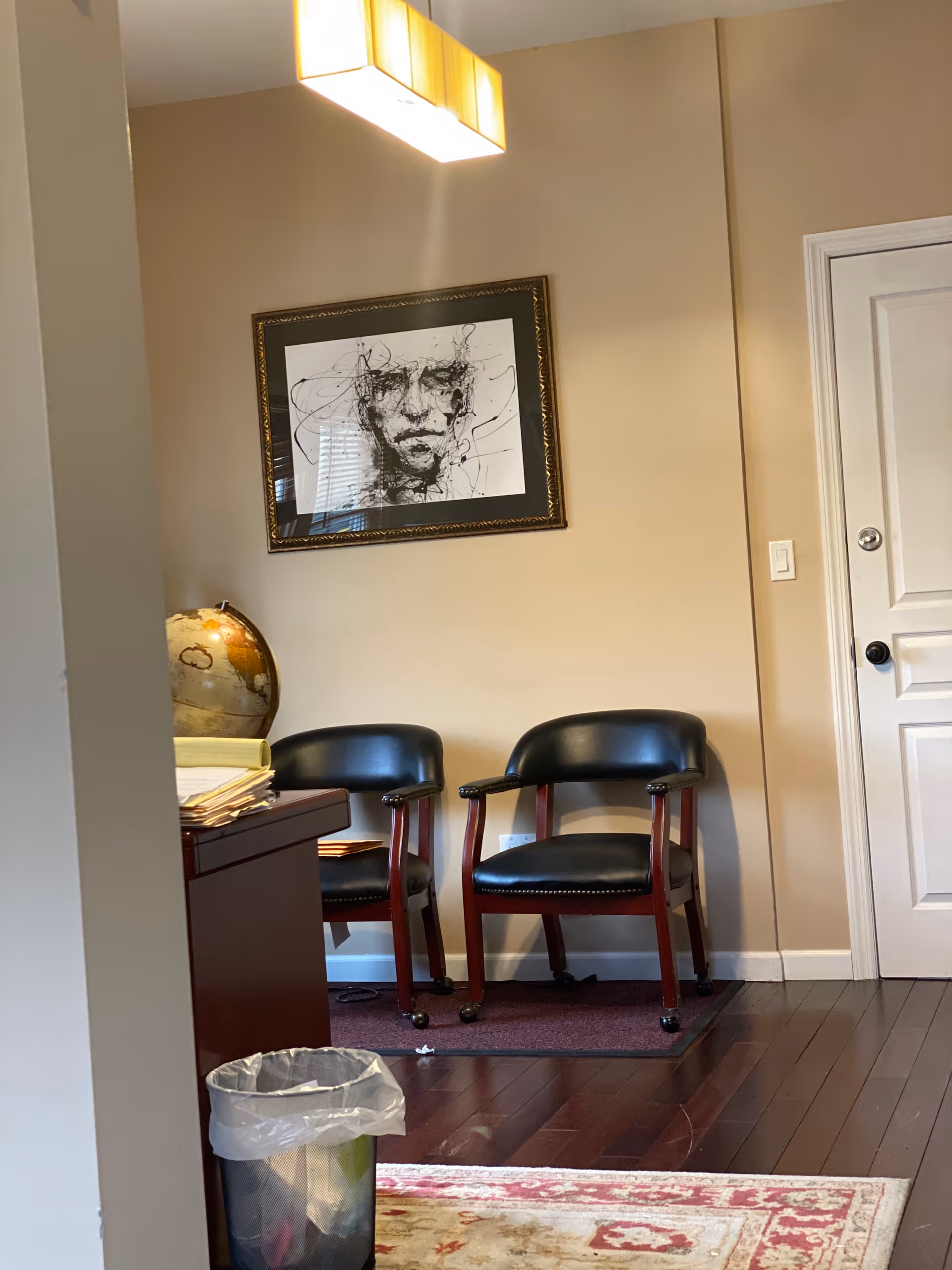 Two black chairs sit in a small waiting area with a globe and framed art.