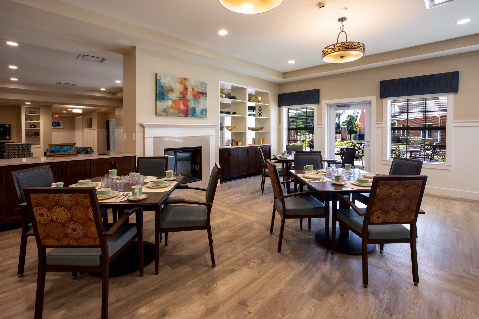 Senior living dining area with tables set for meals, chairs, and windows for natural light.