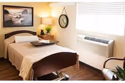 A small bedroom in a senior living facility with a bed and window air conditioner.