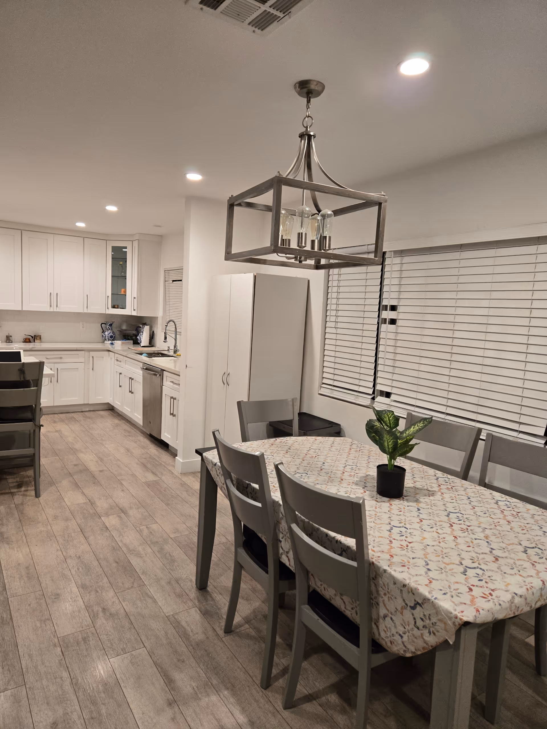 Open-concept kitchen and dining area with a floral tablecloth and potted plant.