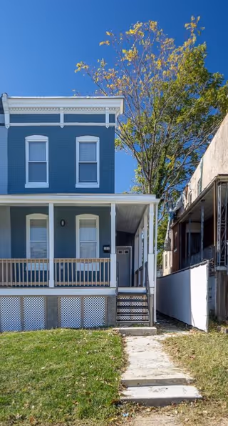 Blue two-story house with a front porch, stairs, and a large tree nearby.