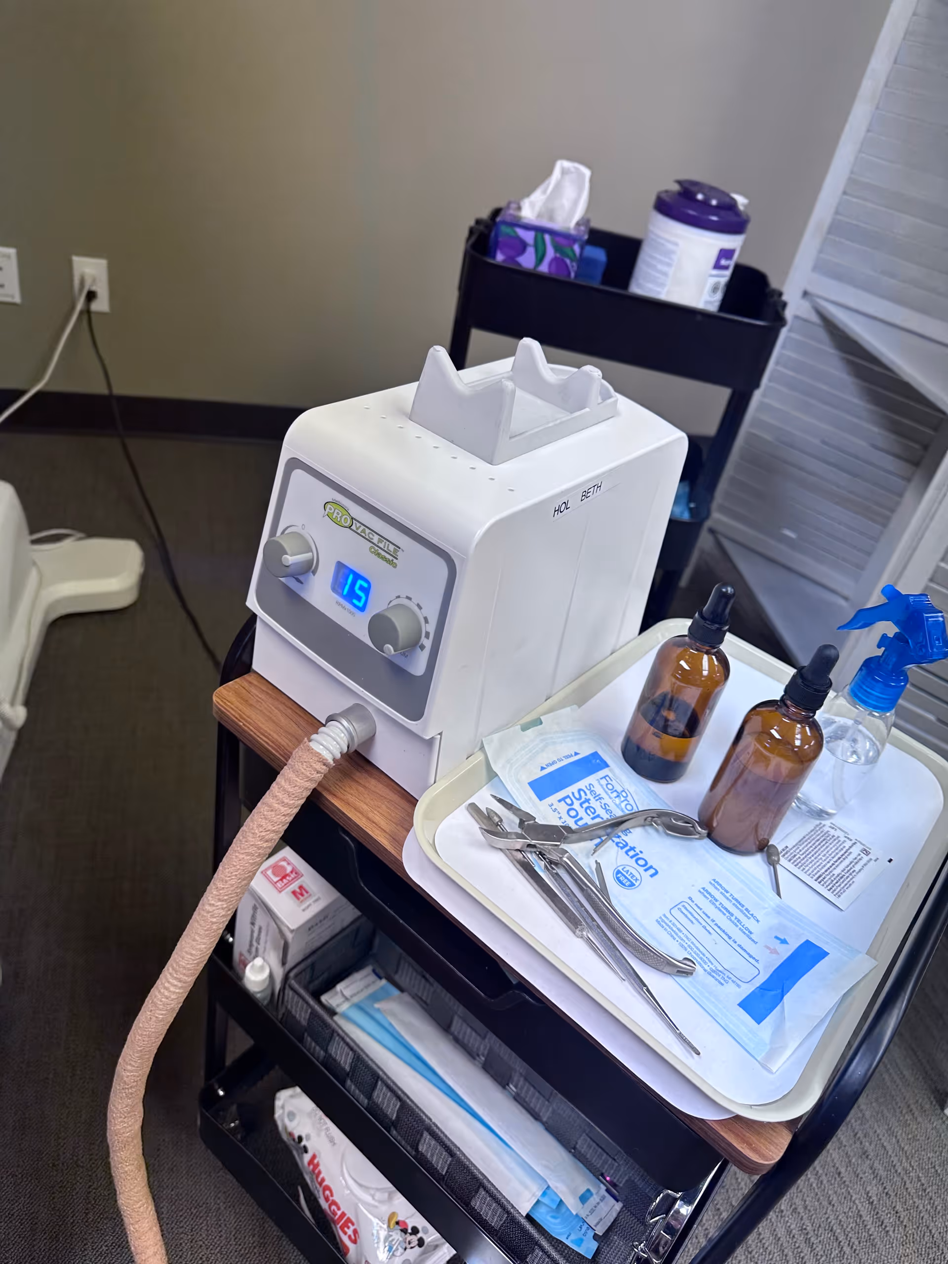 Foot care station with a white medical device, tubes, and nail tools on a wheeled cart.